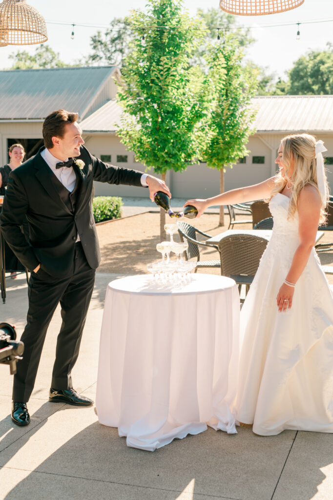 Anna & Codey pour champagne over the tower of glasses in the courtyard of the Historic Barn at Jorgensen Farms.